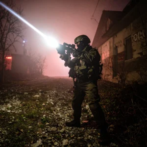 A person holding a new 2025 tactical flashlight, its powerful beam cutting through steam on a city street at night. The image has a cinematic, low-angle perspective.