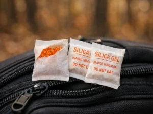 Reusable color-indicating silica gel packets resting on camera bag in Northern Michigan forest — how to protect camera gear hiking with moisture absorbers tested by Outdoor Tech Lab